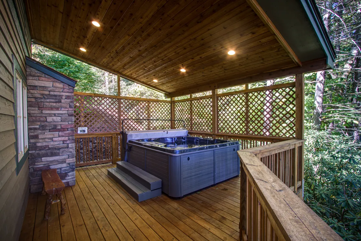 An outdoor deck with a 6-person hot tub set against a backdrop of surrounding greenery, wooden railings, and tranquil forest views. The scene exudes peace and offers a prime spot for soaking, socializing, or enjoying nature.