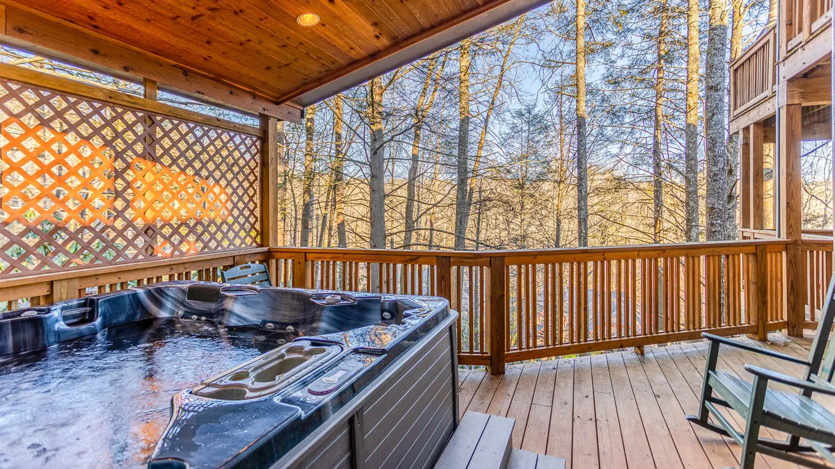 This image features a hot tub set on a wooden deck, surrounded by trees that offer privacy and a tranquil view of nature. The setting is intimate yet spacious enough for groups, capturing the essence of relaxation and shared moments after a day exploring the area.