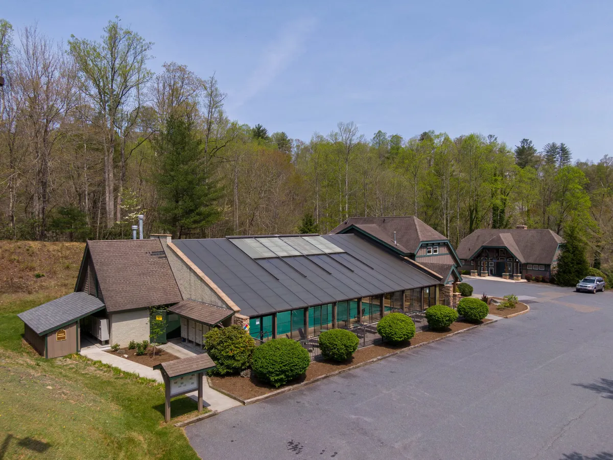 This exterior image features the main building of Bearfoot Lodge, highlighted by large windows that invite in natural light. The lodge is set amidst lush greenery with a visible parking area, emphasizing its tranquil and inviting mountain setting. The surrounding landscape hints at the outdoor activities available in the area.