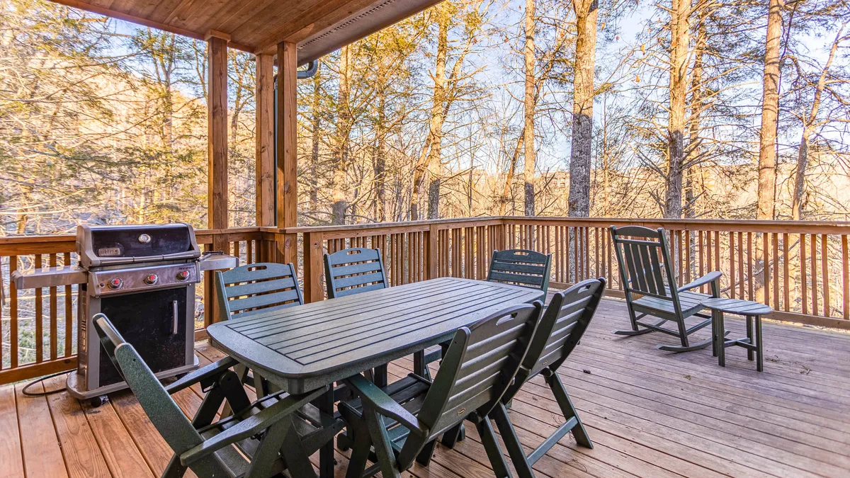 This image showcases a cozy outdoor dining area with a grill and a table set amidst tall trees, perfect for al fresco meals and family barbecues. The tranquil forest backdrop enhances the sense of connection with nature.