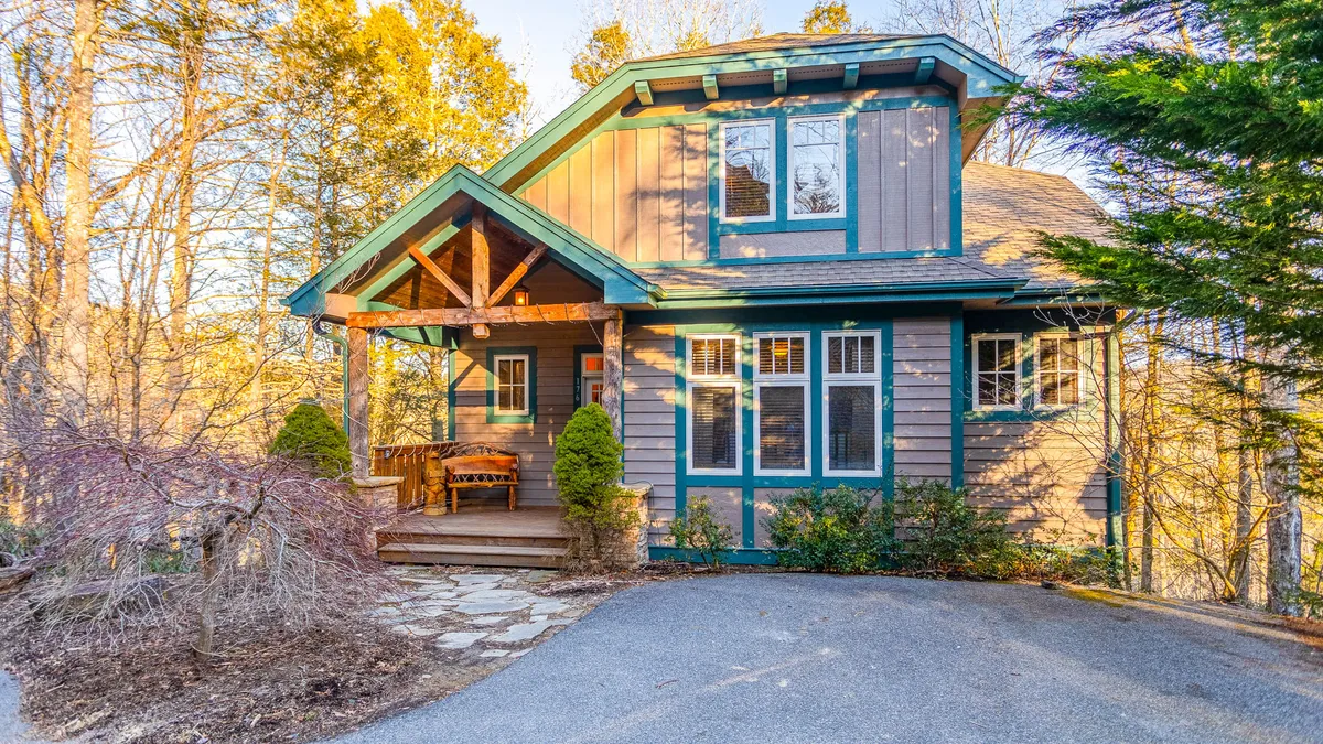 A picturesque exterior shot featuring the lodge's inviting front porch, large windows, a sturdy wooden bench, and carefully maintained landscaping. The scene radiates tranquility and creates a welcoming first impression, suggesting a serene environment for morning coffee or evening relaxation while overlooking the mountains.