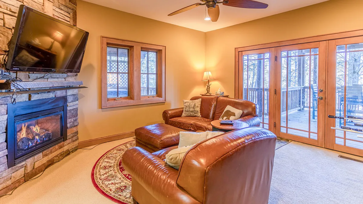 A cozy living room with a fireplace, leather sofas, decorative rug, and windows looking out, creating an inviting space for gathering, socializing, and enjoying the snowy outdoors from inside.