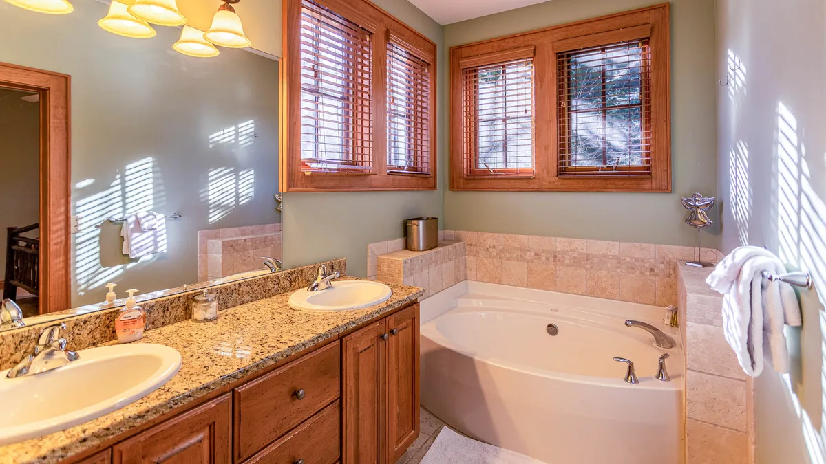 A serene bathroom featuring double vanity sinks and a freestanding bathtub, framed by wooden window accents. The space is bright, clean, and designed for relaxation and self-care.