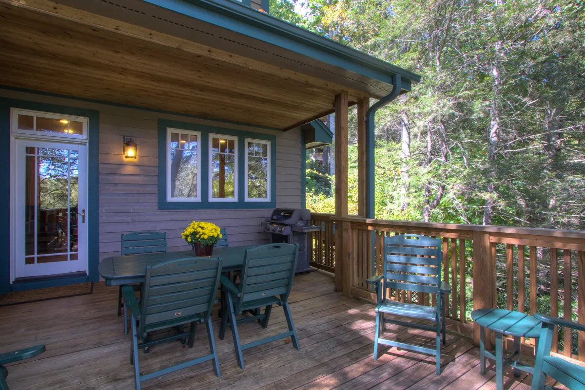 This image features an exterior dining table with chairs set on a deck, surrounded by vibrant yellow flowers and equipped with a grill. The scene is bathed in warm light, suggesting the pleasant outdoor atmosphere ideal for meals, celebrations, and relaxation throughout the year.