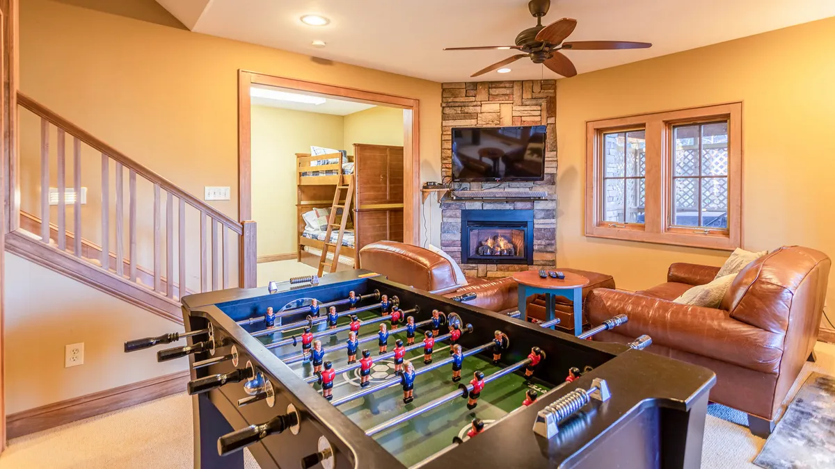 A lower-level entertainment zone with a foosball table, leather sofa, stone fireplace, and a television. The playful yet cozy setting offers both gaming options and a comfortable spot for unwinding or watching TV.