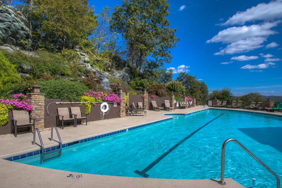 An inviting outdoor pool surrounded by lush greenery, comfortable loungers, and vibrant flowers set the scene for relaxation and fun under the sun. The mood is serene, with guests enjoying swimming, sunbathing, and socializing in a picturesque mountain resort setting.