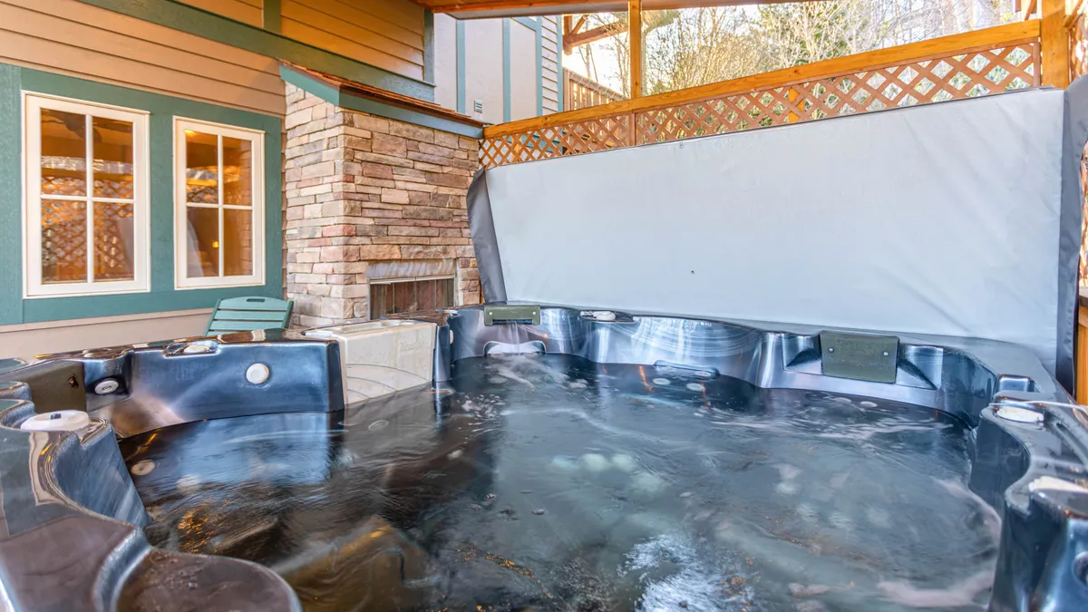 A serene interior scene featuring a private hot tub set against a stone wall with large windows looking out to the natural landscape. The space is bathed in soft light and designed for relaxation, blending indoor luxury with the beauty of the outdoors.